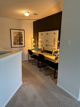 A cozy workspace with dual desks, modern art, and warm lighting on soft carpet flooring.