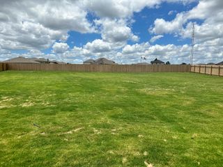 A spacious backyard with green grass, privacy fence, and blue skies in MorningStar by Meritage Homes (Georgetown, TX).