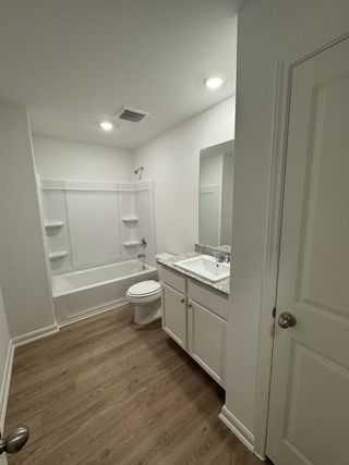 A sleek bathroom featuring wood-look flooring, a white vanity with granite countertop, and a bright, modern shower.
