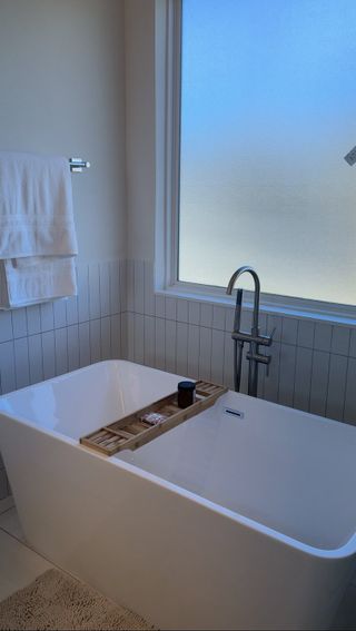 A modern bathroom with a freestanding tub, wall tiles, and a frosted window offering natural light.