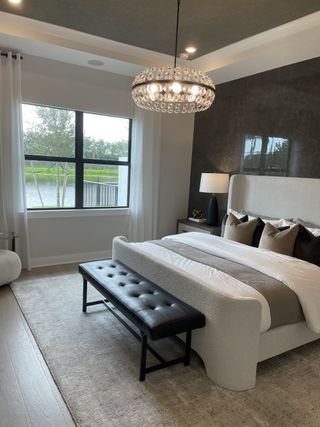 A luxurious bedroom featuring a plush bed, elegant tufted bench, and a stunning chandelier with serene water views.