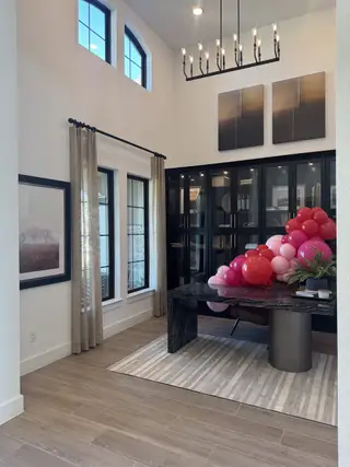A stylish room with modern lighting, a sleek black cabinet, and a decorative table adorned with colorful balloons.