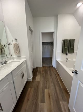 A modern bathroom with sleek wood flooring, dual sinks, and a spacious tub leading to a walk-in closet.