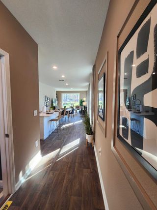 Model Home A modern hallway with hardwood floors, framed art, and a view into an elegant dining area filled with natural light.