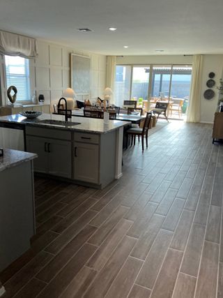 An open-concept living area featuring wood-look tile, modern kitchen, and sunlit dining leading to a spacious patio.
