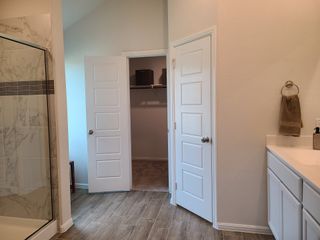 Model Home A modern bathroom featuring a marble-accented shower, wood-style flooring, and sleek white cabinetry.