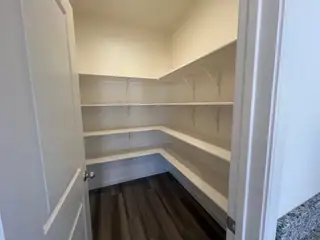 A spacious pantry with open white shelving and sleek dark wood flooring.