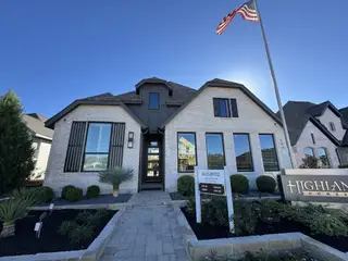 A beautiful white brick home with modern black accents and lush landscaping in 6 Creeks at Waterridge by Highland Homes (Kyle, TX).