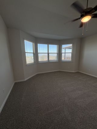 A spacious bedroom with a bay window, neutral carpeting, and a ceiling fan for added comfort.