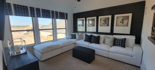 A cozy living room with a sectional sofa, black accent wall, and large windows showcasing ample natural light.