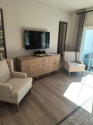 A cozy living area featuring a modern TV setup, elegant wooden sideboard, and two comfortable plaid armchairs.