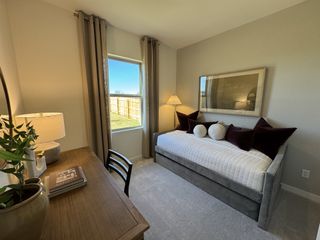A tranquil space featuring a sleek daybed adorned with plush decorative pillows. A wooden desk and chair sit near a window that offers views of the backyard. 