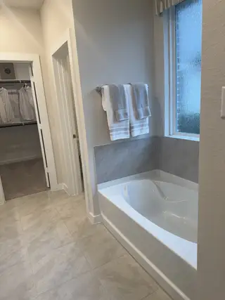 A sleek bathroom featuring a modern bathtub, large window, and adjacent open closet space, offering elegance and functionality.