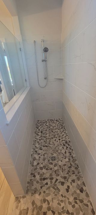 Model Home A sleek, walk-in shower with beautiful marble-tiled walls and a stone pebble floor for a modern touch.