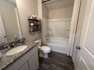 A modern bathroom featuring a granite countertop, sleek shelving, and a clean, tiled shower area.