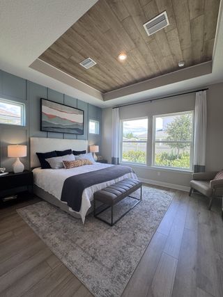A cozy bedroom with wood-paneled ceiling, large windows, and modern decor in neutral tones.