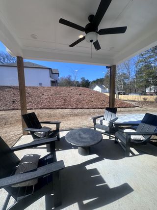 A cozy patio with Adirondack chairs, a ceiling fan, and a round table, perfect for outdoor relaxation.