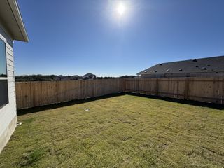 A spacious backyard with wooden fencing and a clear blue sky in Opal Ranch by Brightland Homes (Kyle, TX).