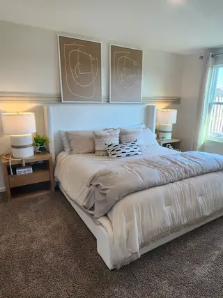 A cozy bedroom with soft carpeting, a decorative accent wall, and natural light in Copes Landing by D.R. Horton (Jacksonville, FL).