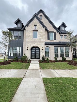 A stunning stone and black-trimmed home with lush landscaping in Edgewater by Grand Homes (Fate, TX).