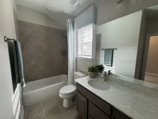 A compact bathroom with a combination tub/shower featuring diamond-patterned tile, a dark wood vanity with a light countertop, and a decorative patterned valance.