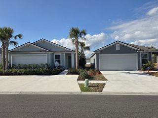 Street view Two single-story homes with siding exteriors and attached garages in Cross Creek by D.R. Horton (Green Cove Springs, FL) feature palm trees and paved driveways.