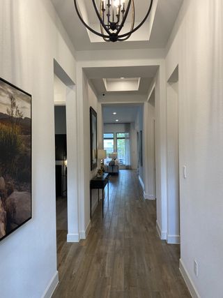 A grand hallway with tray ceilings, wood-look flooring, and elegant lighting leading to an open living area.