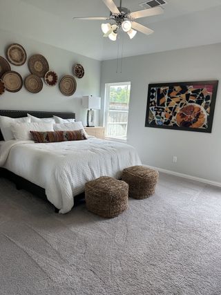 A cozy bedroom featuring a plush bed, woven decor, stylish art, and soft carpeting, creating a warm and inviting atmosphere.