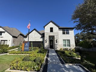 Street view A beautiful stone brick home with lush landscaping in 6 Creeks by Chesmar Homes (Kyle, TX).