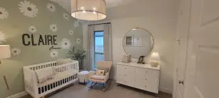 A charming nursery with daisy accents, soft lighting, a white dresser, rocking chair, and personalized wall decor.