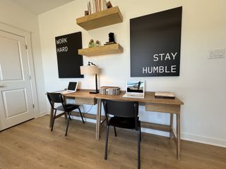 A modern workspace with a wooden desk, dual chairs, and motivational wall art alongside minimalist shelving.