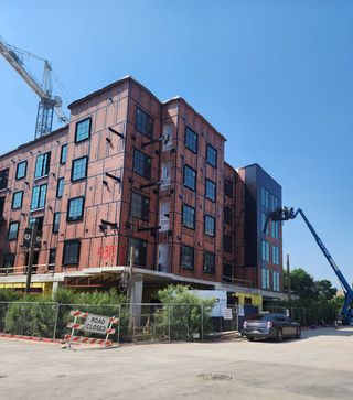 Exterior view of a building in progress with cranes, scaffolding, and bright blue skies at Congress Lofts Saint Elmo by Intracorp (Austin, TX).