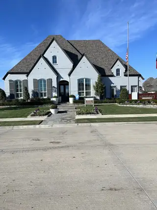Street view A stunning Highland Homes model with a grand entry, steep gables, and a light brick façade. The manicured lawn and stone pathway lead to an inviting front porch.