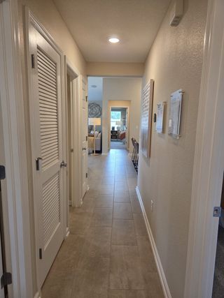 Model Home A modern hallway with sleek tile flooring, neutral walls, and recessed lighting leading to a cozy living space.