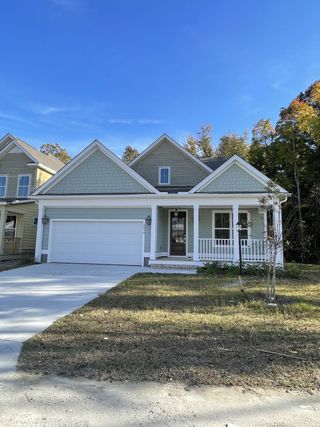 A charming grey home with gabled roof and cozy porch in Overlook at Copahee Sound by Dream Finders Homes (Awendaw, SC).