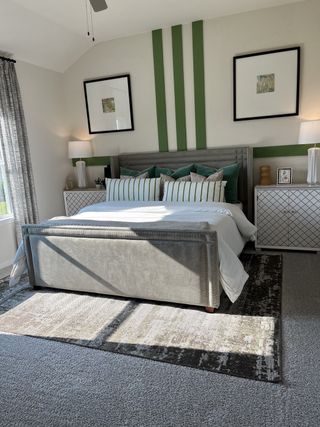 A modern bedroom with patterned bedding, green accent wall, and sleek decor, flooded with natural light.