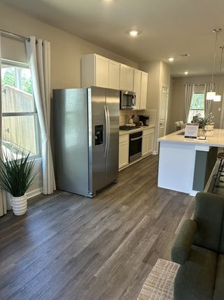 Model Home Modern kitchen with stainless steel fridge, white cabinets, and wood floors under pendant lighting.