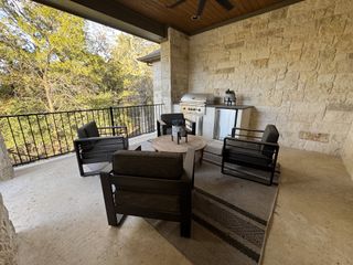 A cozy outdoor patio with a stone wall, comfy seating, and a built-in grill under a wooden ceiling. Ideal for relaxation.