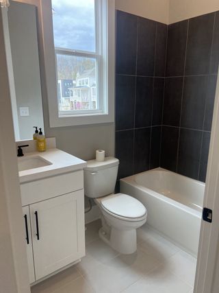 A modern bathroom featuring a sleek white vanity, tub, and contrasting dark tile accents.