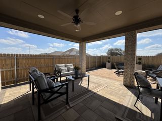Model Home A cozy covered patio with cushioned seating, ceiling fan, and a fenced outdoor area, perfect for relaxation.