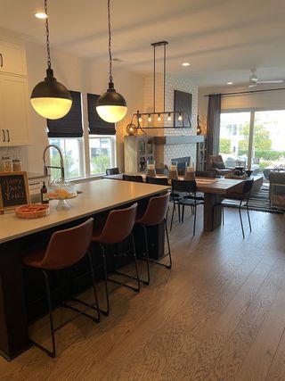 A modern kitchen and living area featuring a sleek island, pendant lighting, a cozy fireplace, and elegant wood flooring.