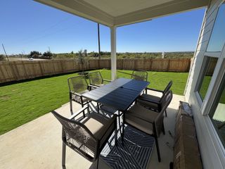 A cozy patio with a modern dining set, overlooking a lush, fenced backyard and scenic views.