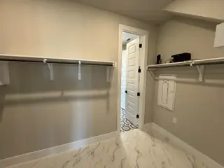 Model Home A spacious walk-in closet with marble-tile flooring and sturdy shelving, leading to a room with patterned tiles.