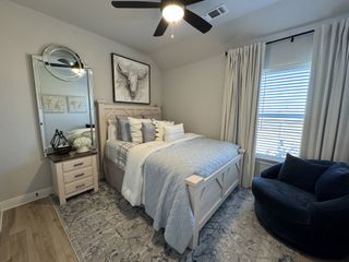 A cozy bedroom featuring a plush bed, elegant mirror, and soft armchair, accented by serene gray tones and natural light.