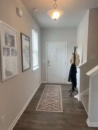 An inviting hallway features wood floors, a decorative runner, and stylish lighting, leading to a cozy, well-organized entrance.