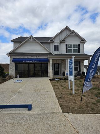 Street view A beautifully designed model home with white siding, black shutters, and a spacious driveway in Clark Farms by McKinley Homes (Flowery Branch, GA).