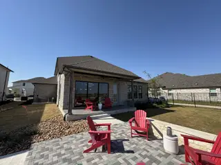 Model Home A relaxing outdoor patio with red Adirondack chairs and a stone fire pit in Blackhawk by GFO Home (Pflugerville, TX).