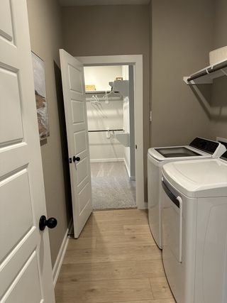A functional laundry room with modern washer and dryer, light wood floors, and access to a walk-in closet.