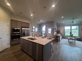 A spacious, modern kitchen and living area with an island, stainless appliances, and wide windows overlooking a green yard.