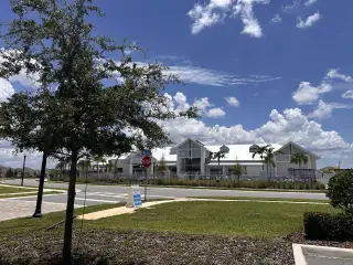 A contemporary clubhouse with palm trees and a bright sky in Del Webb Oasis by Del Webb (Winter Garden, FL).